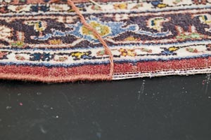 Teppichkante im Vorher-Nachher Vergleich. Links die in Handarbeit neu umstochene Kante, rechts der noch durch starke Beanspruchung ausgefranste Teppichrand.